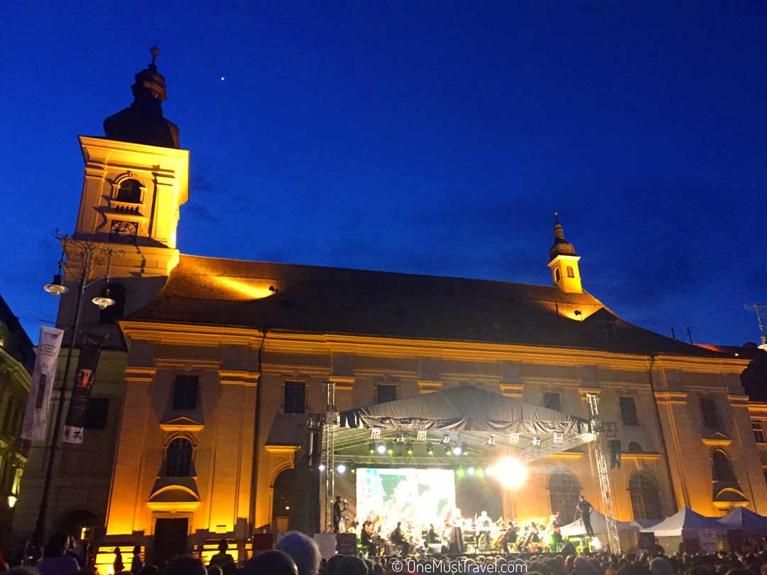 A concert lit up at night in front of a historic building in Sibiu. 