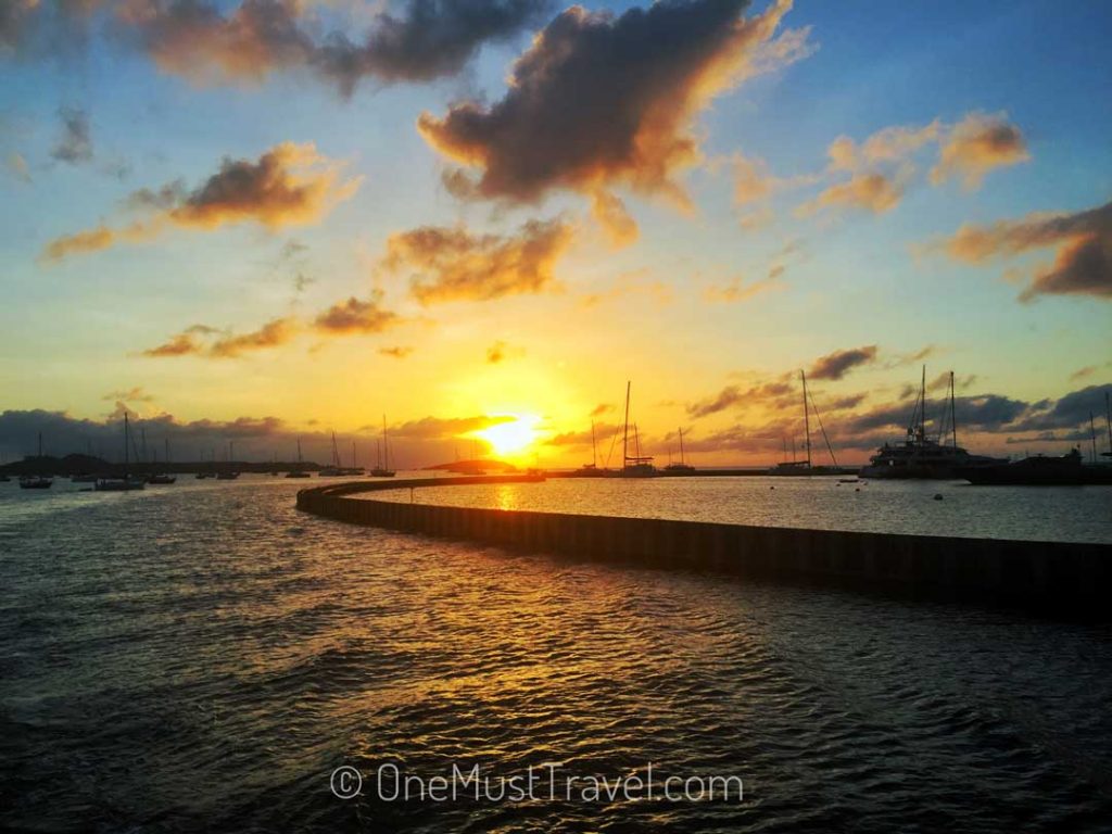 The sun setting over Marigot Bay in St. Martin. The clouds are illuminated orange set against the blue sky.